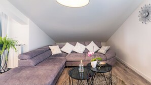 A modern living room with a sectional sofa, a glass bottle, a potted plant, and a wall clock. - Apartments Mladenka 2 (Rab)