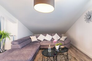 A modern living room with a sectional sofa, a glass bottle, a potted plant, and a wall clock. - Apartments Mladenka 2 (Rab)
