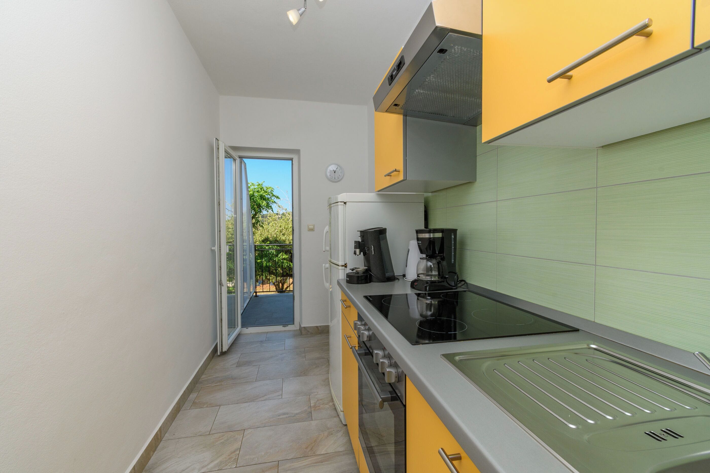 A narrow kitchen with a stove, coffee maker, and a view of the outdoors.
