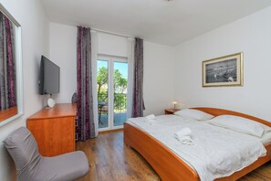 A hotel room with a bed, a desk, a chair, a TV, and a balcony with curtains. - Apartments Mladenka 2 (Rab)