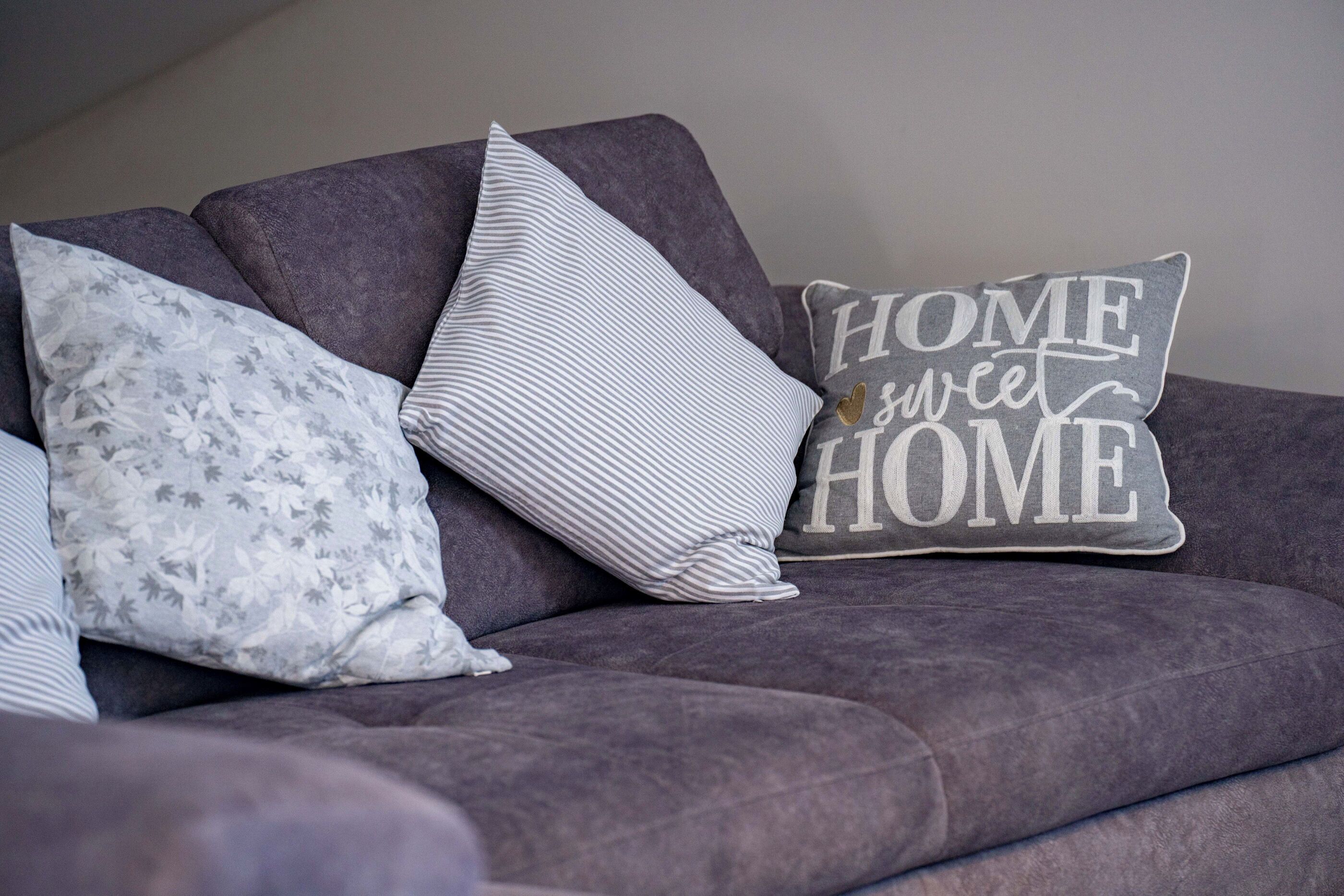 A grey sofa with three pillows, one with a floral pattern, one striped, and one with 'HOME sweet HOME' text.