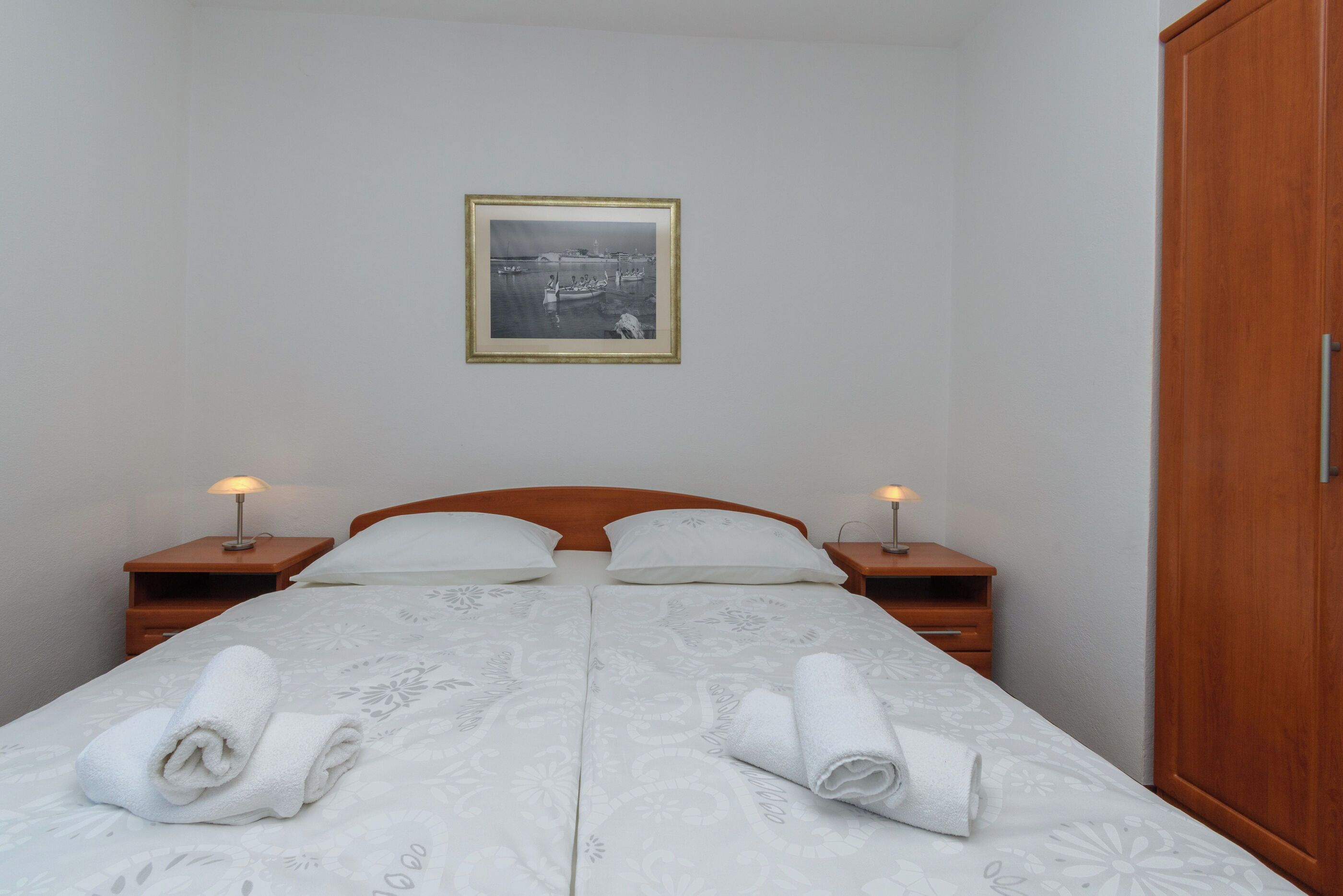 A double bed with two nightstands, a wooden wardrobe, and a framed picture on the wall.