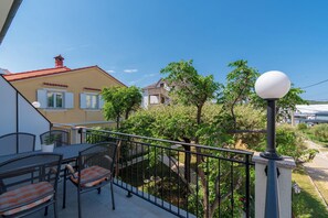 A balcony with outdoor furniture, a railing, and a street view with houses and trees. - Apartments Mladenka 2 (Rab)
