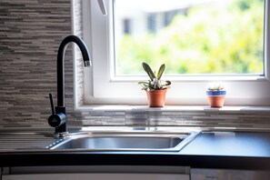 A kitchen with a modern faucet, a window with a view of greenery, and two potted plants on the windowsill. - Apartments Mladenka 2 (Rab)