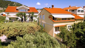A residential area with houses featuring red-tiled roofs, white walls, and green landscaping. - Apartments Mladenka 2 (Rab)