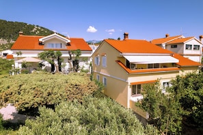 A residential area with houses featuring red-tiled roofs, white walls, and green landscaping. - Apartments Mladenka 2 (Rab)