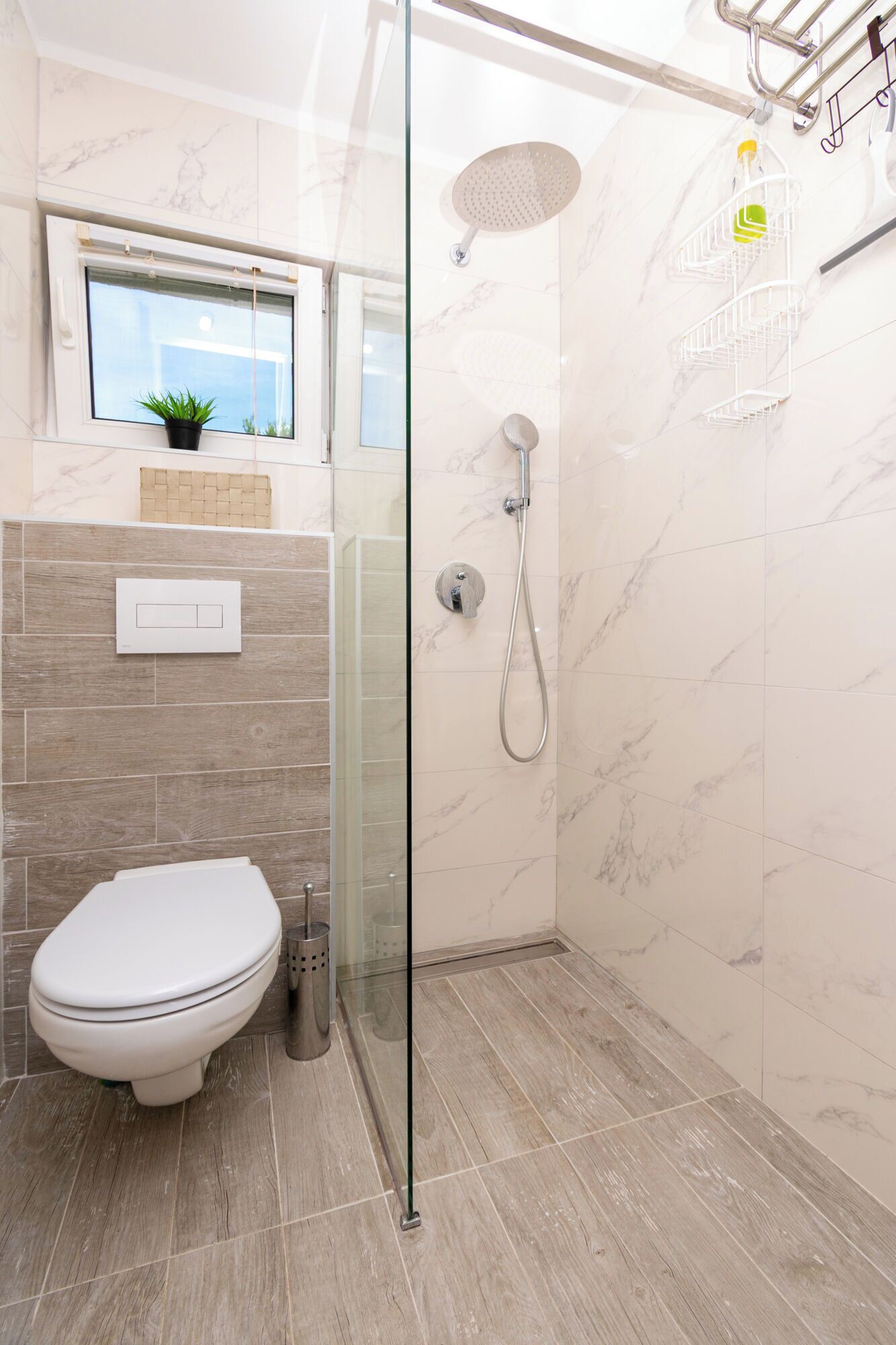 Ein modernes Badezimmer mit Duschkabine aus Glas, Toilette und kleinem Fenster mit Pflanze.