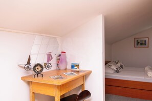 A bedroom with a wooden desk, a bed with pillows, a framed picture on the wall, and a small table with a vase and magazines. - Apartments Andrijana (Starigrad)