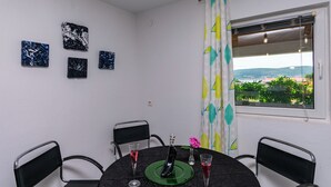 Un comedor con una mesa redonda, cuatro sillas, una botella, dos vasos y una obra de arte en la pared.