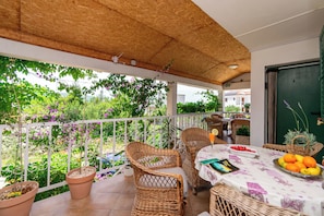 Eine überdachte Terrasse mit Korbmöbeln, einem Tisch mit Früchten und Topfpflanzen.