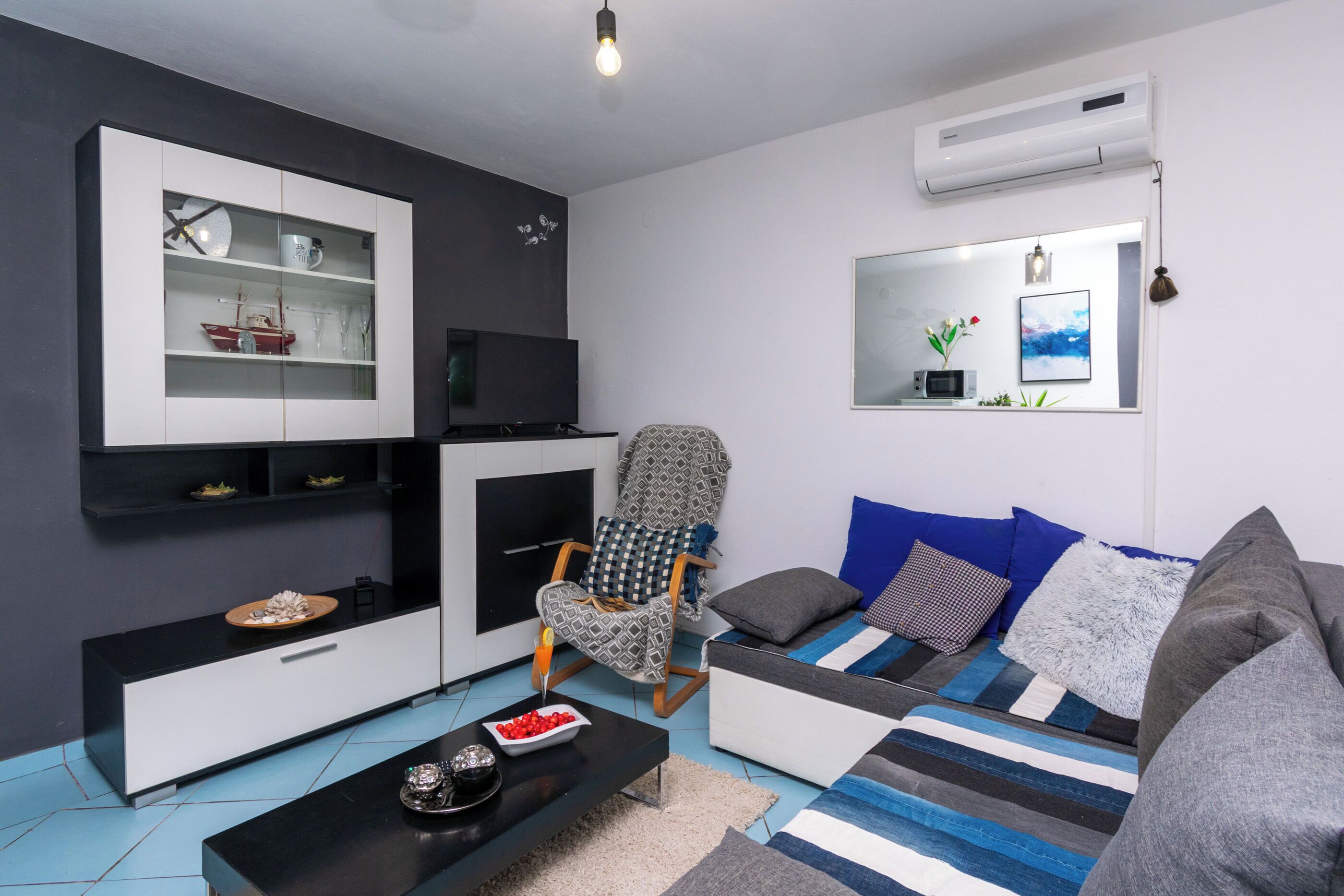 A modern living room with a sofa, a black coffee table, a patterned armchair, a flat-screen TV, and a built-in cabinet with shelves.