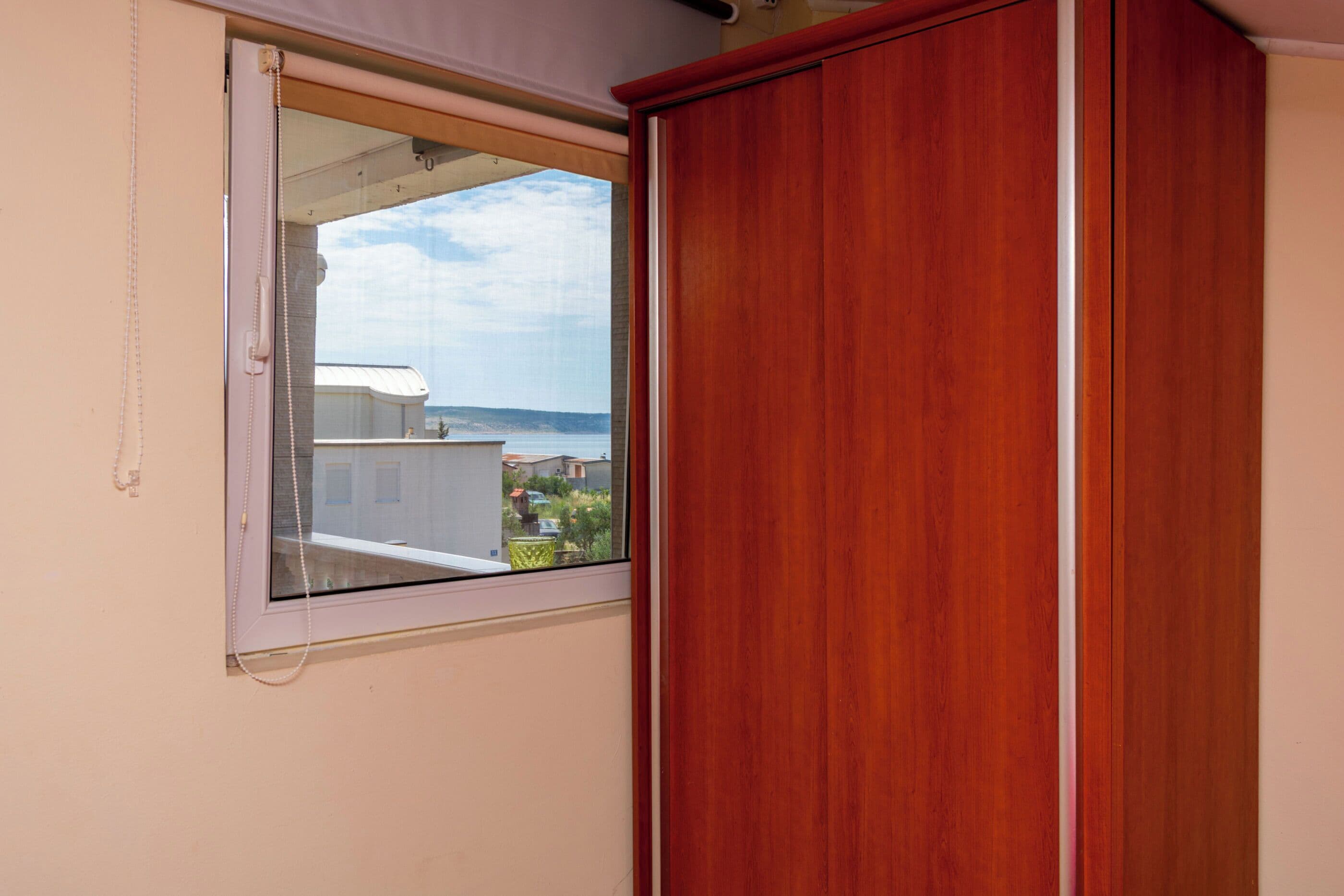 Una habitación con un armario de madera, una ventana con vista a edificios y una masa de agua.
