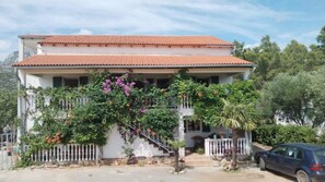 A two-story house with a tiled roof, a balcony with plants, and a parked car. - Apartments Andrijana (Starigrad)