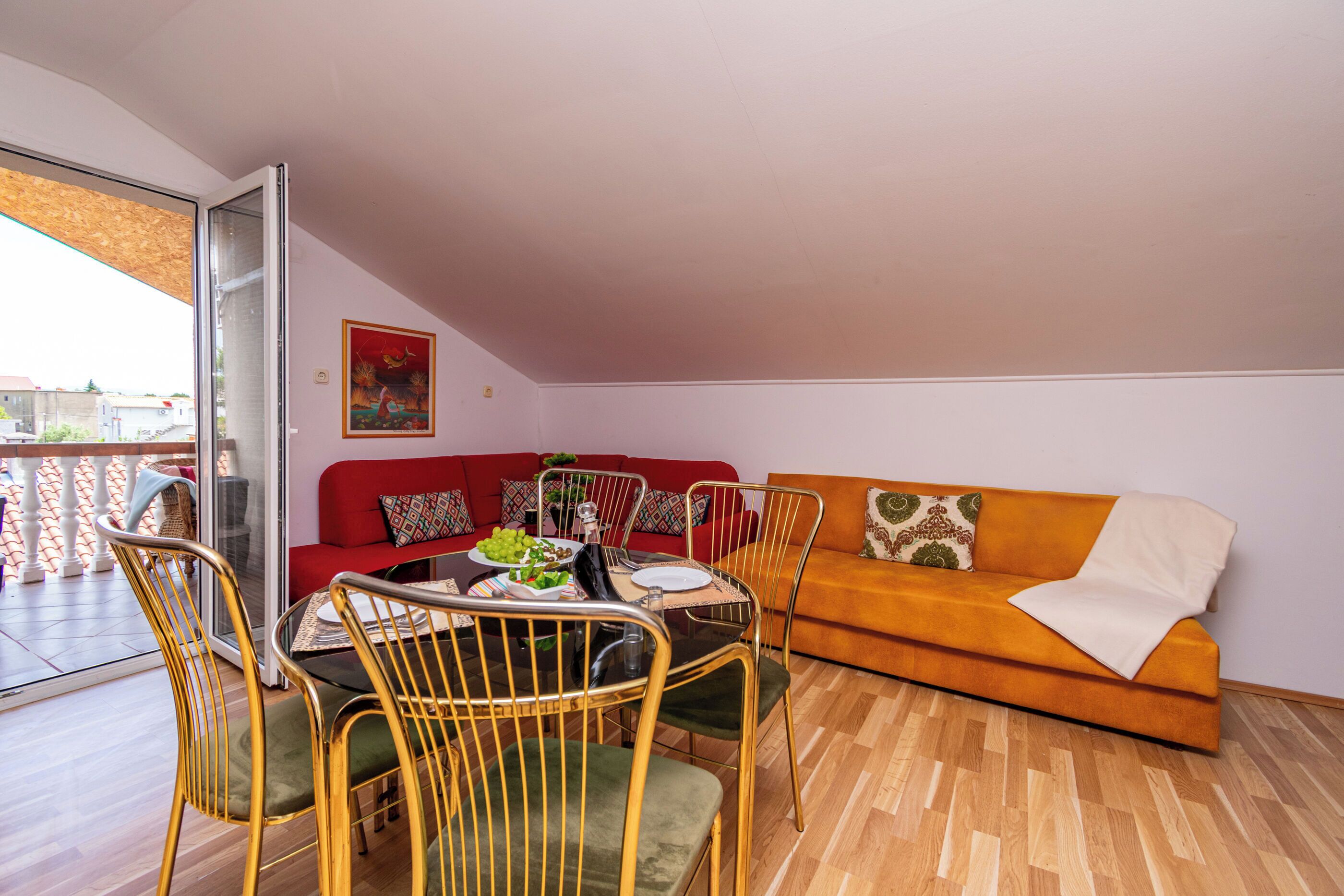 A dining area with a table set for two, a red sofa, and an orange sofa in a room with wooden flooring.