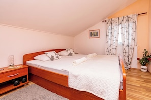 Un dormitorio con cama de madera, una mesita de noche, una ventana con cortinas y un cuadro enmarcado en la pared.