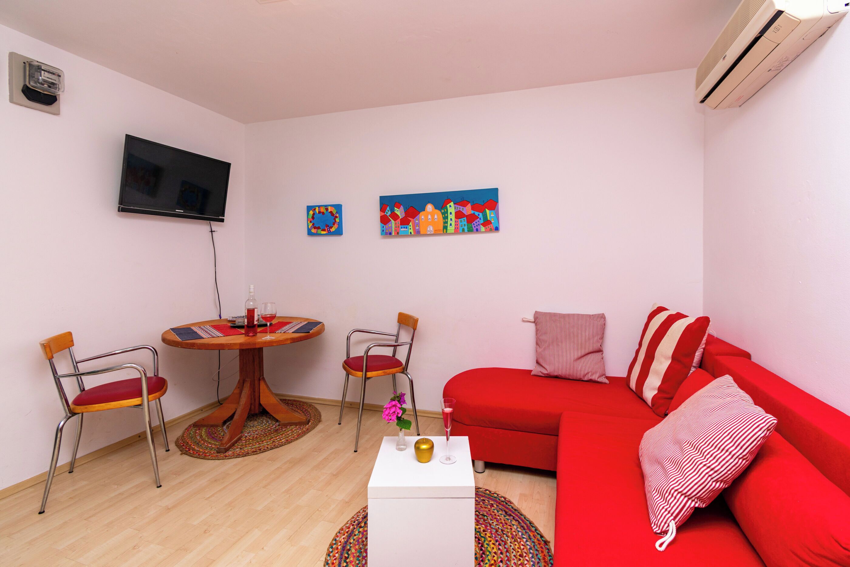 A living room with a red sofa, two chairs, a small table with a vase and a glass, and two paintings on the wall.