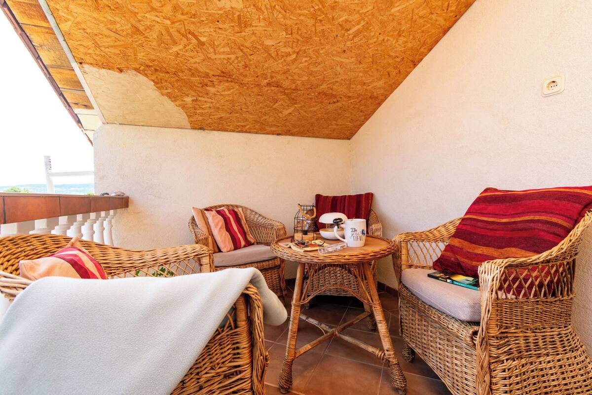 Ein Sitzbereich im Freien mit Korbmöbeln, einem runden Tisch, Stühlen und einem kleinen Tisch mit Tasse und Buch.