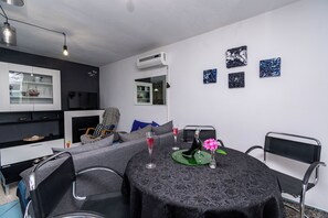 Ein modernes Wohnzimmer mit Essbereich, darunter ein runder Tisch mit Stühlen, eine Couch und ein Fernseher.