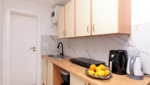 Una cocina con un lavamanos, una cafetera, un hervidor y un bol de fruta en la encimera.