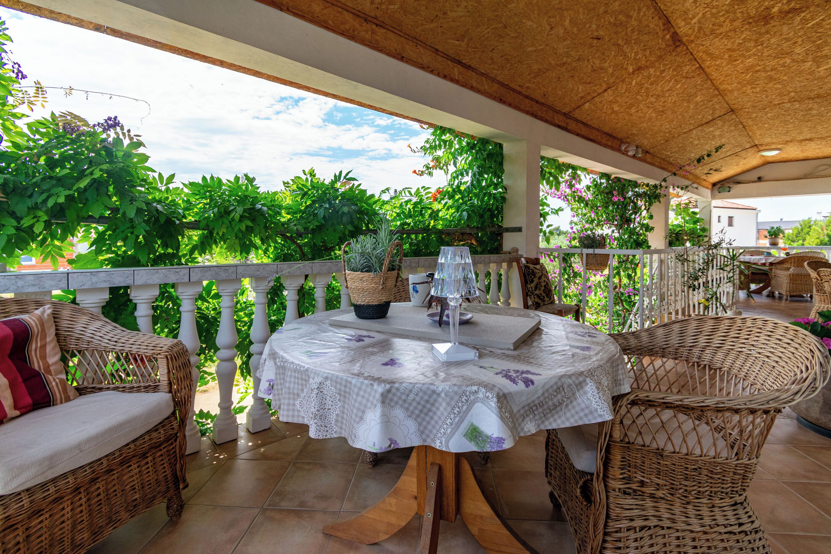 Un patio al aire libre con mobiliario de mimbre, una mesa redonda con mantel y plantas en macetas.
