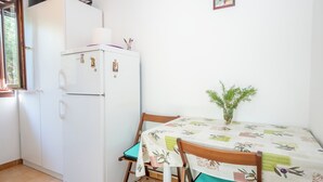 Uma cozinha compacta com geladeira, mesa de jantar com cadeiras e um pequeno vaso de planta.