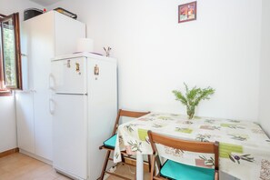A compact kitchen with a refrigerator, a dining table with chairs, and a small potted plant. - Apartments Olive and Sea (Solta)