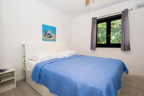 A bedroom with a bed, a nightstand, a window with curtains, and a wall-mounted air conditioning unit. - Apartments Olive and Sea (Solta)