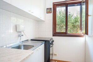 A kitchen with a sink, a stove, and a window with a view of trees. - Apartments Olive and Sea (Solta)