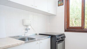 Uma cozinha com armários brancos, uma pia de aço inoxidável, um fogão e uma janela com vista para árvores.