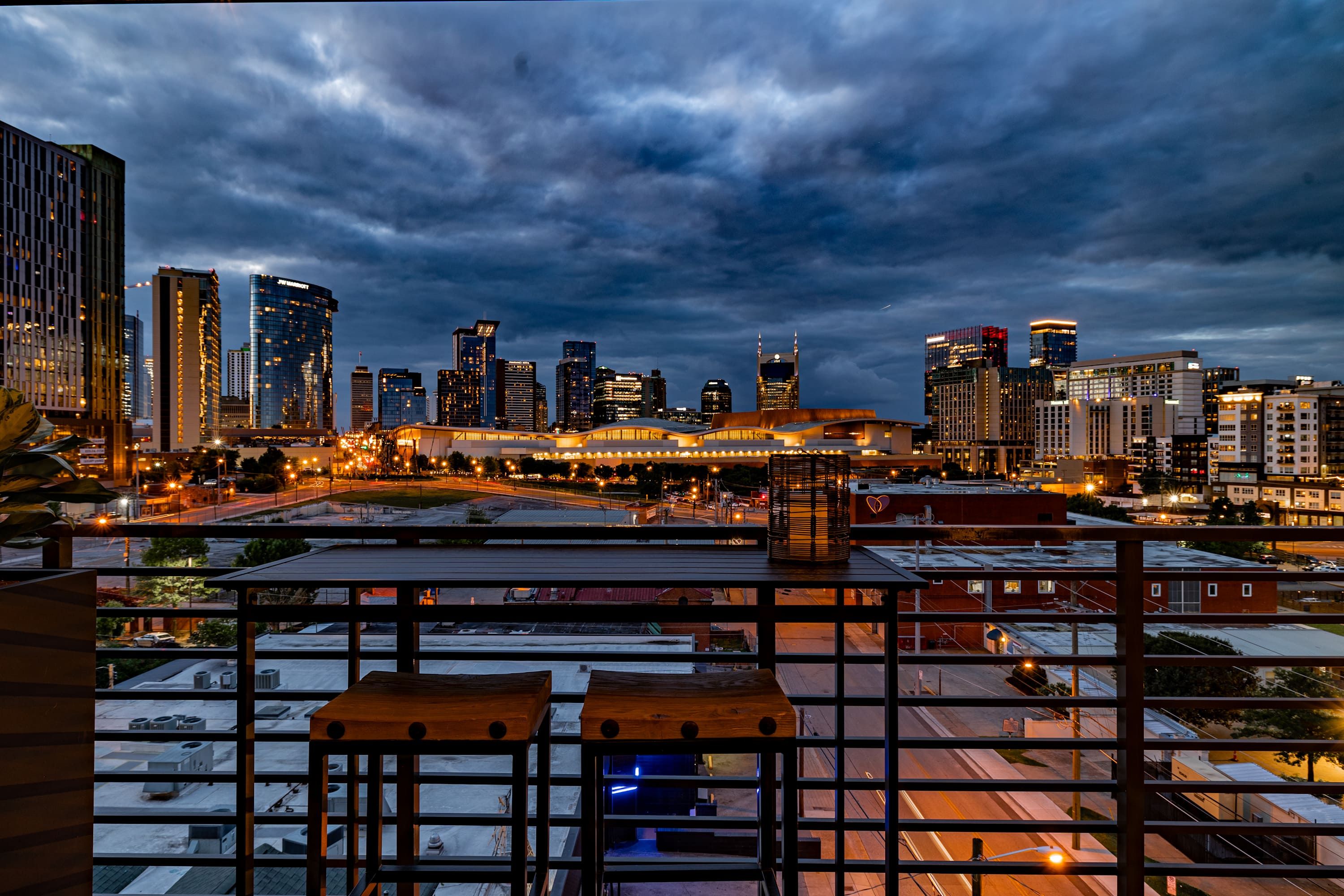 A city skyline at dusk with modern buildings and a large, illuminated structure in the center.