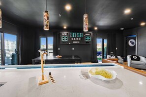 A modern indoor pool area with a digital scoreboard, seating, and a view of the city. - Neon & Nashville | 8BR, Pool Table, Balconies (Nashville)