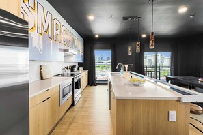 A modern kitchen with wooden cabinets, stainless steel appliances, and a large island with a sink. - Neon & Nashville | 8BR, Pool Table, Balconies (Nashville)