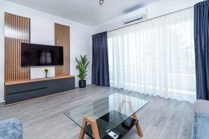 Ein modernes Wohnzimmer mit Flachbildfernseher, Glastisch, Sofa und einer Topfpflanze.