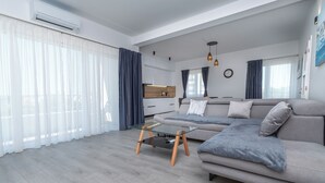 Ein modernes Wohnzimmer mit einer Couch, einem Glastisch und einer Küche im Hintergrund.