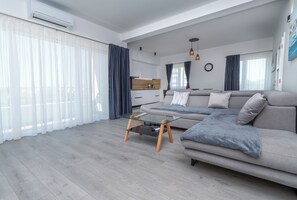 A modern living room with a sofa, a glass coffee table, and a kitchen in the background. - Apartment Rooftop Valerija (Okrug)