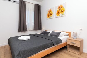 A bedroom with a bed, a bedside table with a lamp, a nightstand, and two wall-mounted paintings. - Apartment Rooftop Valerija (Okrug)