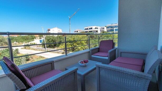 Ein Balkon mit Korbmöbeln, einem Tisch und einer Obstschale.
