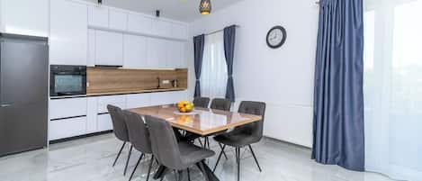 A modern kitchen with white cabinets, a wooden countertop, and a dining table with chairs.