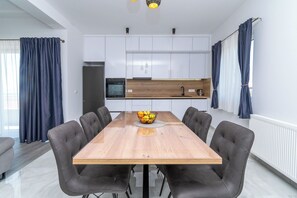 A modern kitchen with white cabinets, a wooden dining table, and a fruit bowl. - Apartment Rooftop Valerija (Okrug)