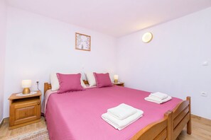 Un llit ben fet amb roba de llit rosa, dues taules de nit amb làmpades i un llum de paret.