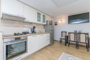 A modern kitchen with stainless steel appliances, a dining area with wooden chairs, and a flat-screen TV mounted on the wall. - House Romance for two (Lovreć)