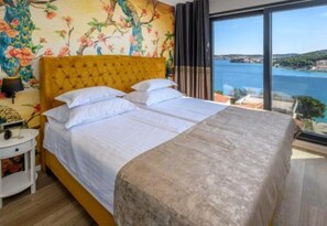 Ein Bett mit Kopfteil, ein Nachttisch mit Lampe und Blick auf das Meer.