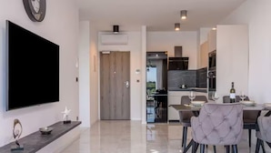 A modern kitchen with dark cabinets, a dining area with a table and chairs, and a flat-screen TV mounted on the wall. - Apartments Penthouse Lux (Rogoznica)