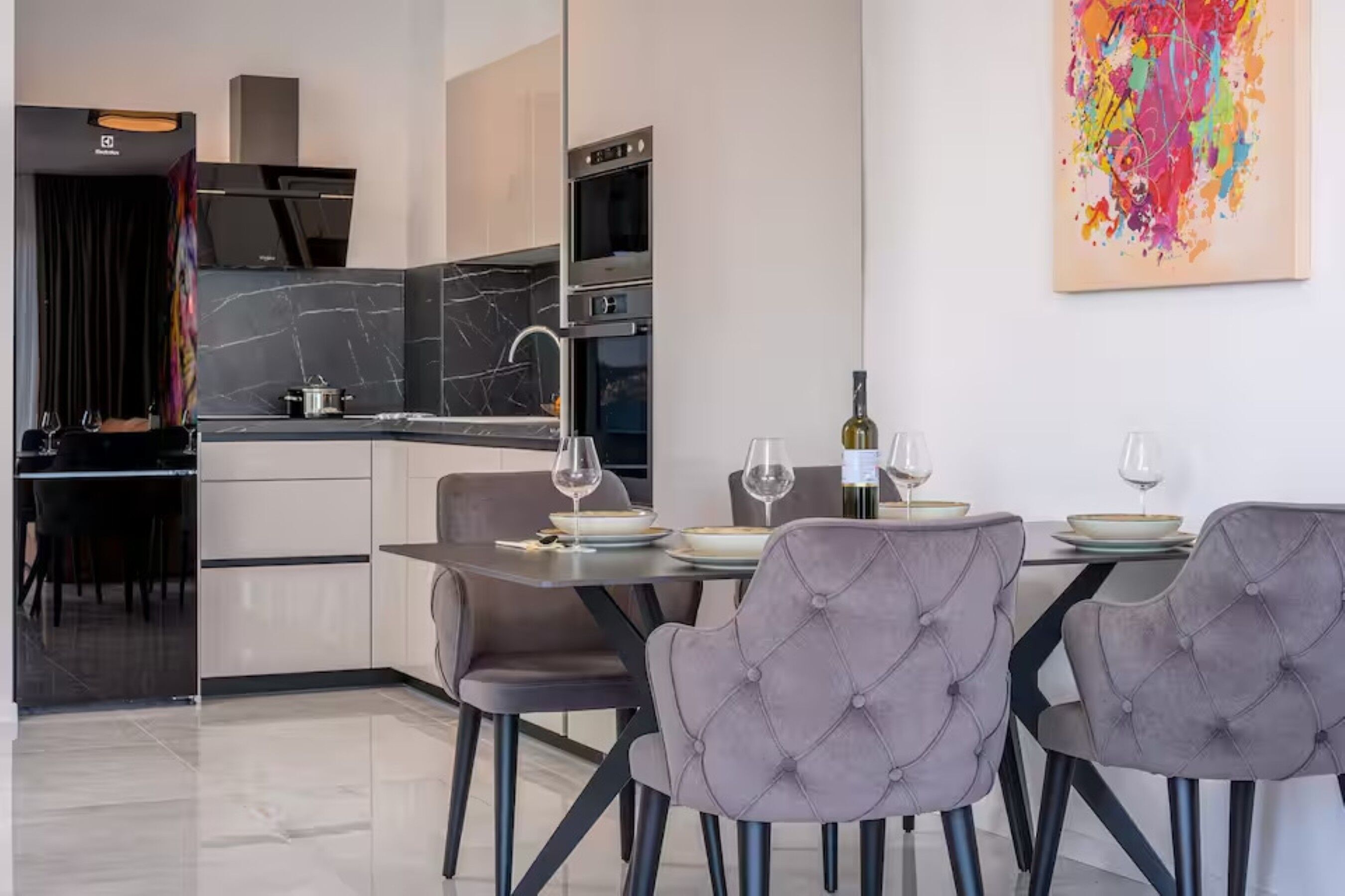 A modern kitchen with a dining area, featuring a marble backsplash, stainless steel appliances, and a contemporary art piece.
