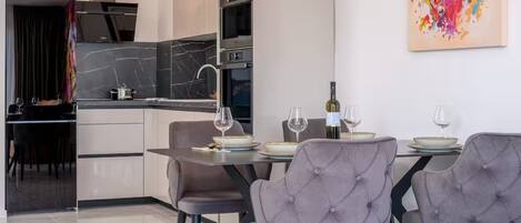 A modern kitchen with a dining area, featuring a marble backsplash, stainless steel appliances, and a contemporary art piece.