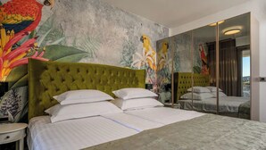 A hotel room with a large bed, a green upholstered headboard, a mural with tropical birds, and a large mirror reflecting the room. - Apartments Penthouse Lux (Rogoznica)