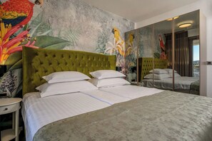 A hotel room with a large bed, a green upholstered headboard, a mural with tropical birds, and a large mirror reflecting the room. - Apartments Penthouse Lux (Rogoznica)