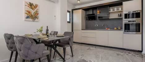 A modern kitchen with built-in appliances, a dining area with grey upholstered chairs, and a marble floor.