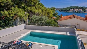 A rectangular swimming pool with lounge chairs and a view of a coastal town. - Apartments Penthouse Lux (Rogoznica)