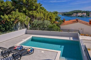 A rectangular swimming pool with lounge chairs and a view of a coastal town. - Apartments Penthouse Lux (Rogoznica)